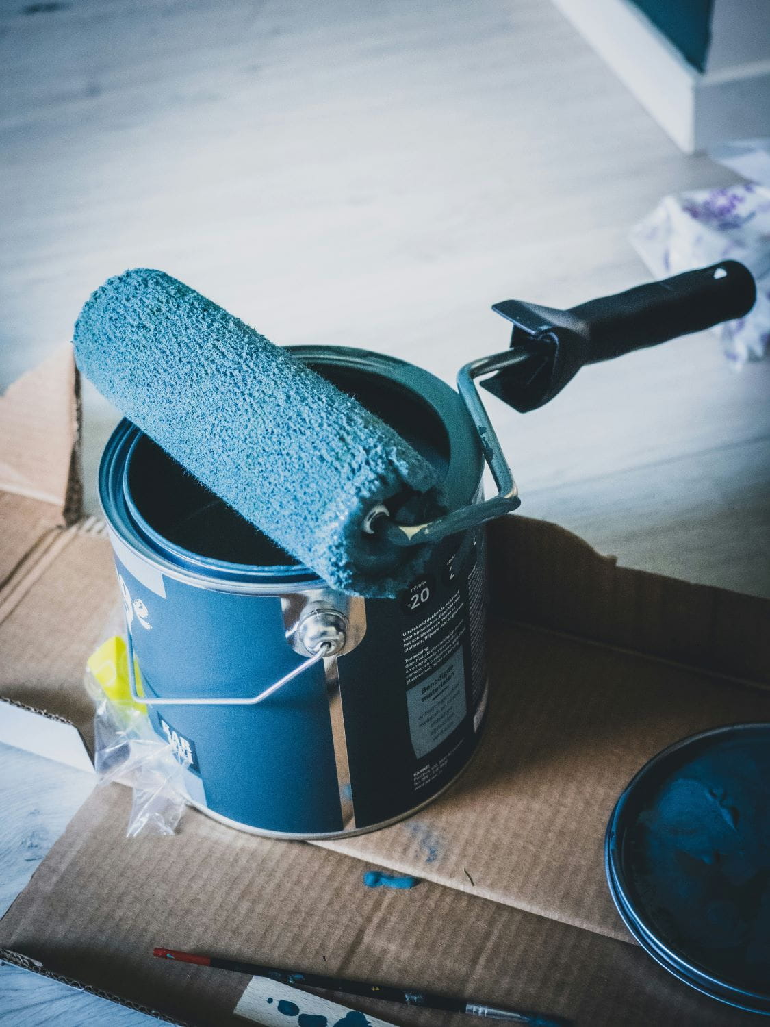 An open can of blue paint with a used paint roller resting on top