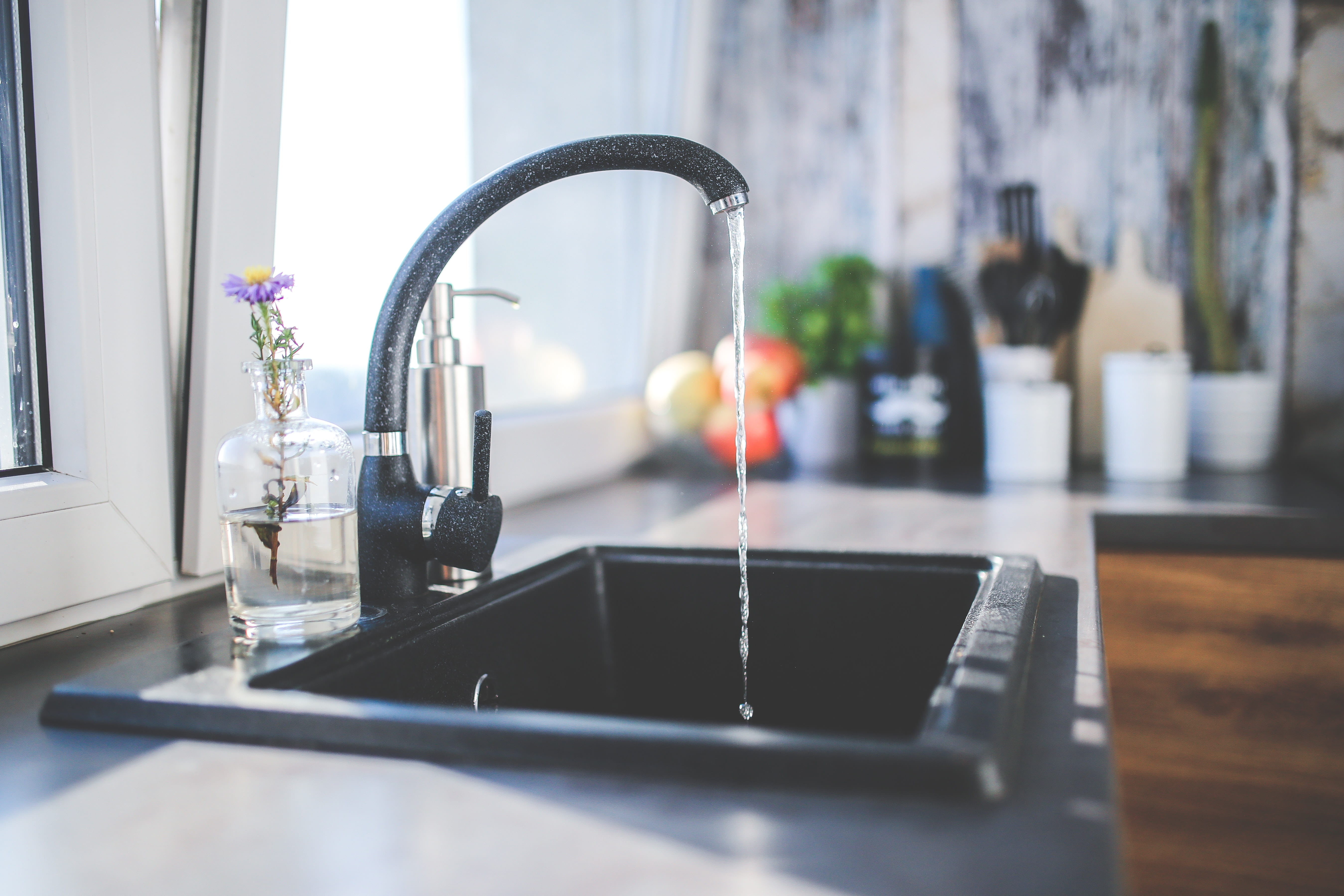 A kitchen faucet on a dark countertop with clear water running into the sink