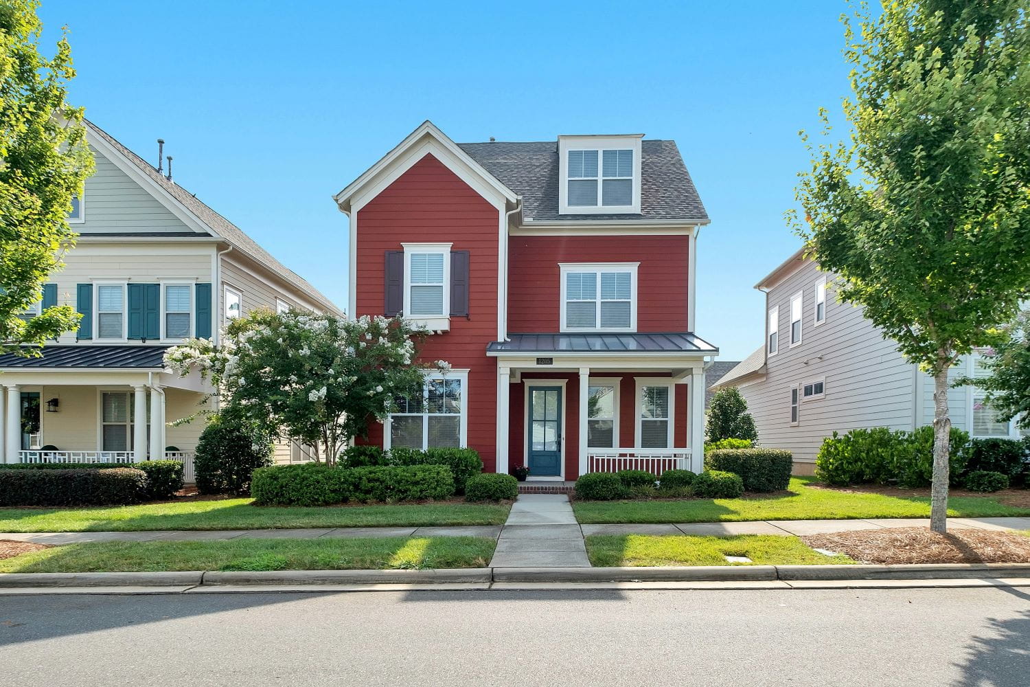 A bright red two-story house nestled between two other homes on a residential street on a bright summer day