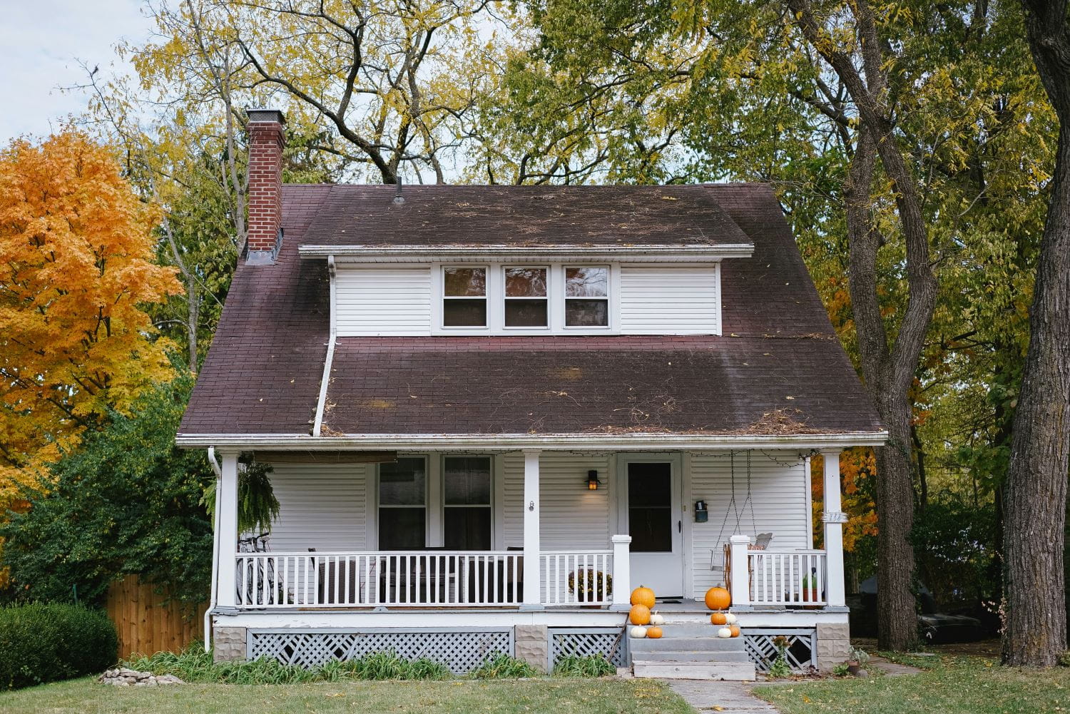 A white two-story house with a large porch decorated for fall with pumpkins on the steps