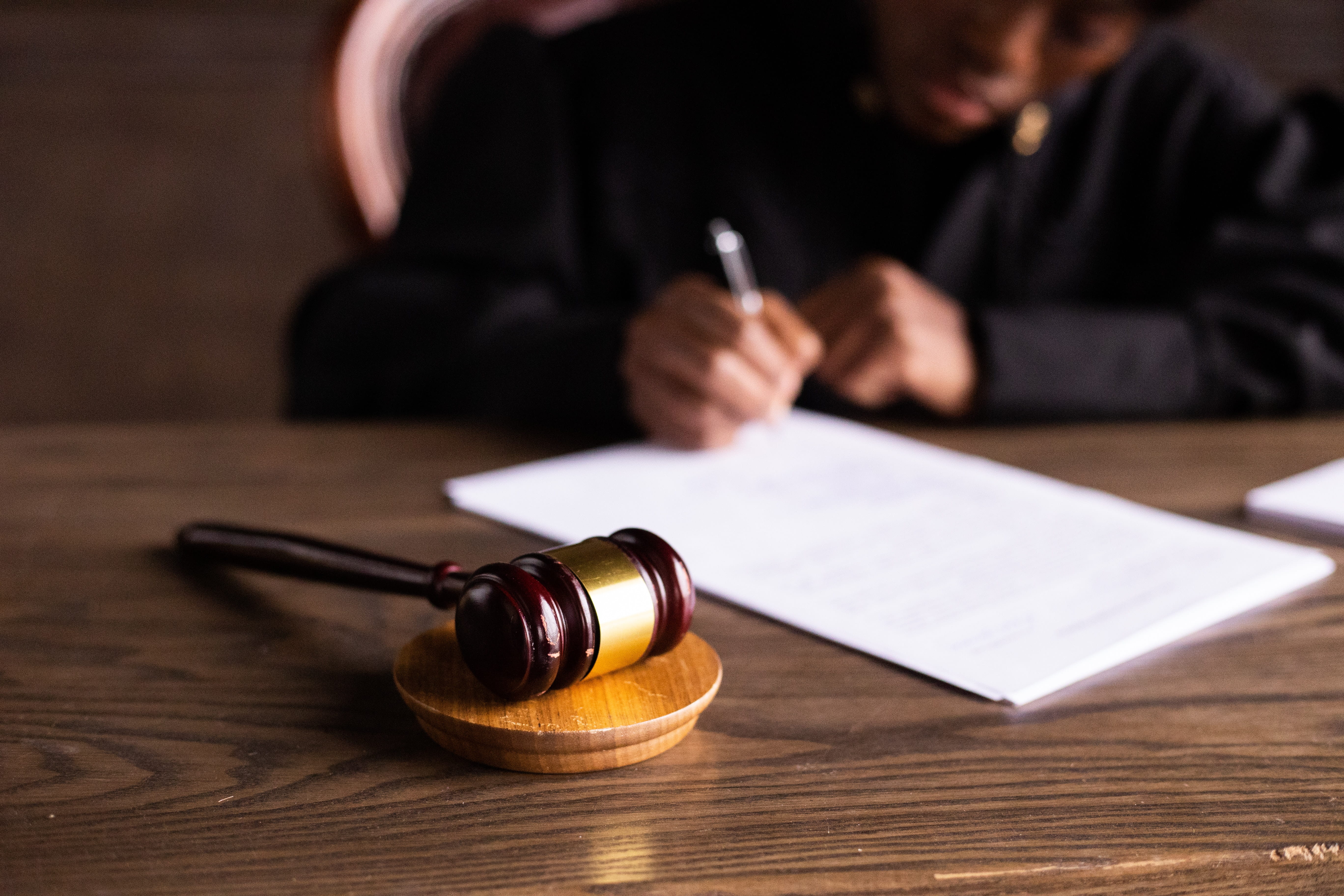 An African-American judge signs a piece of paper at at wooden surface, with a gavel laying nearby