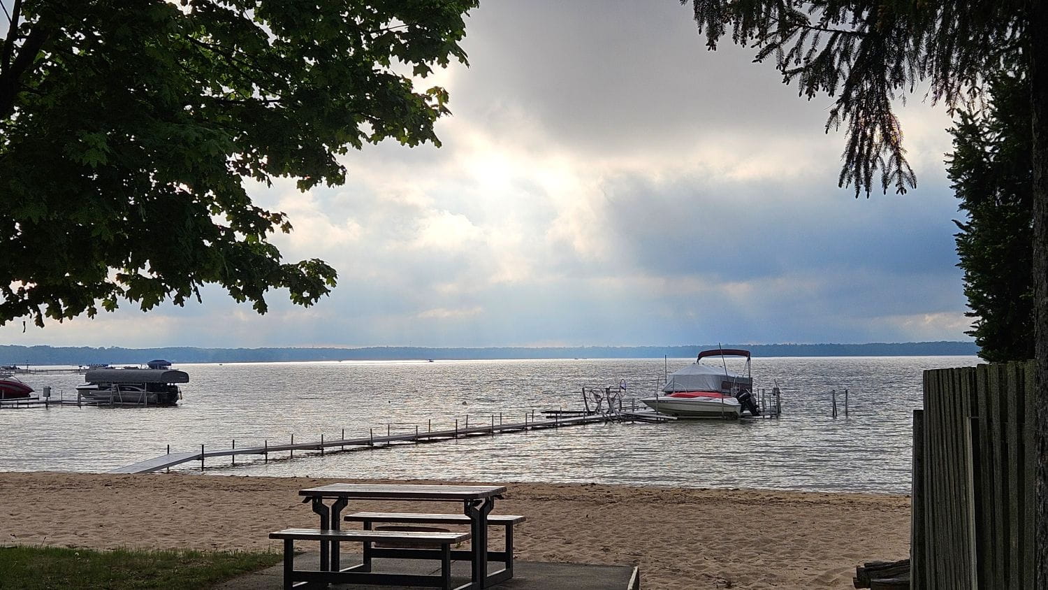 Lake Missaukee showing the beach, a dock and boats on a cloudy day.