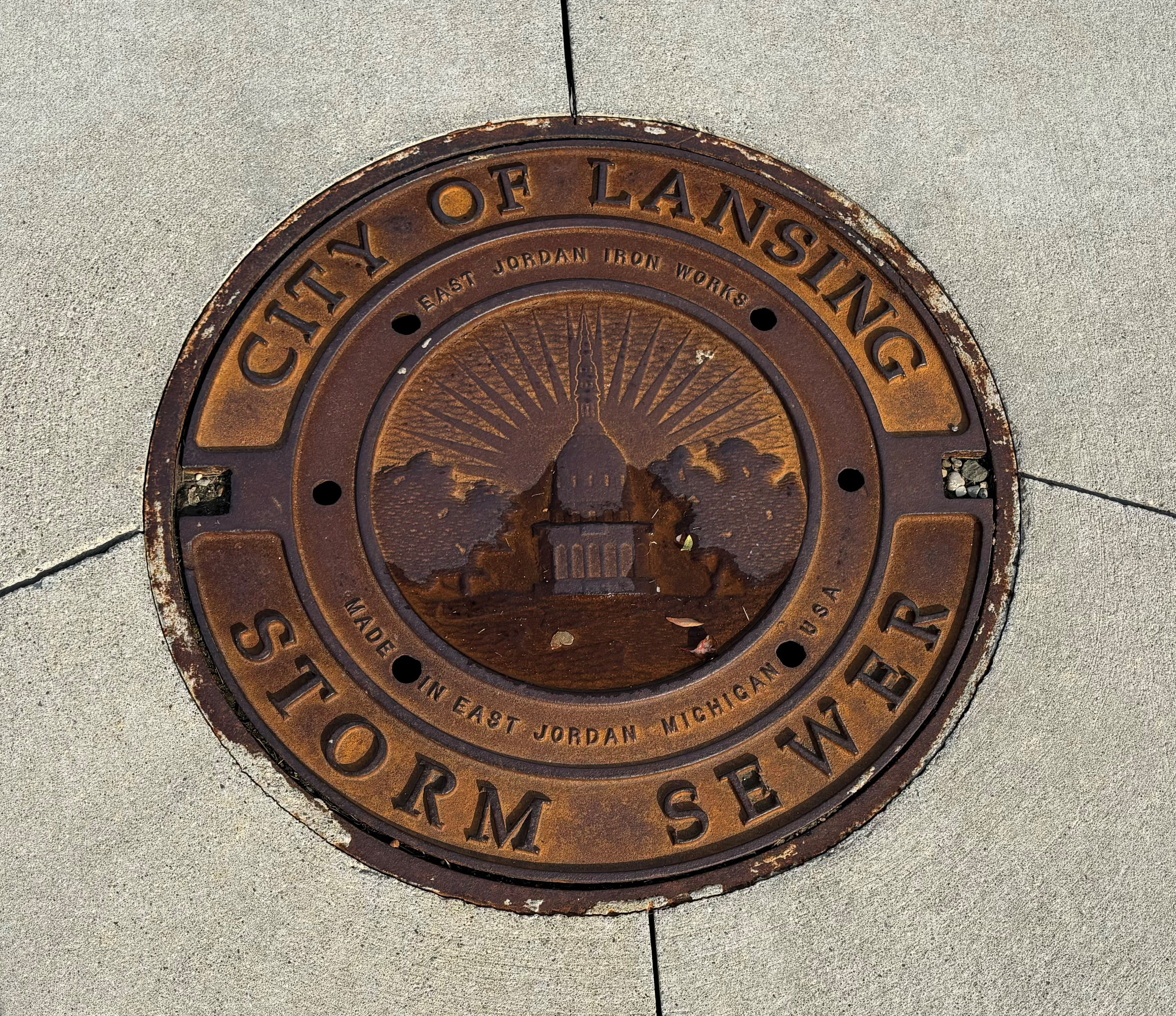 A brown metal City of Lansing storm sewer cover