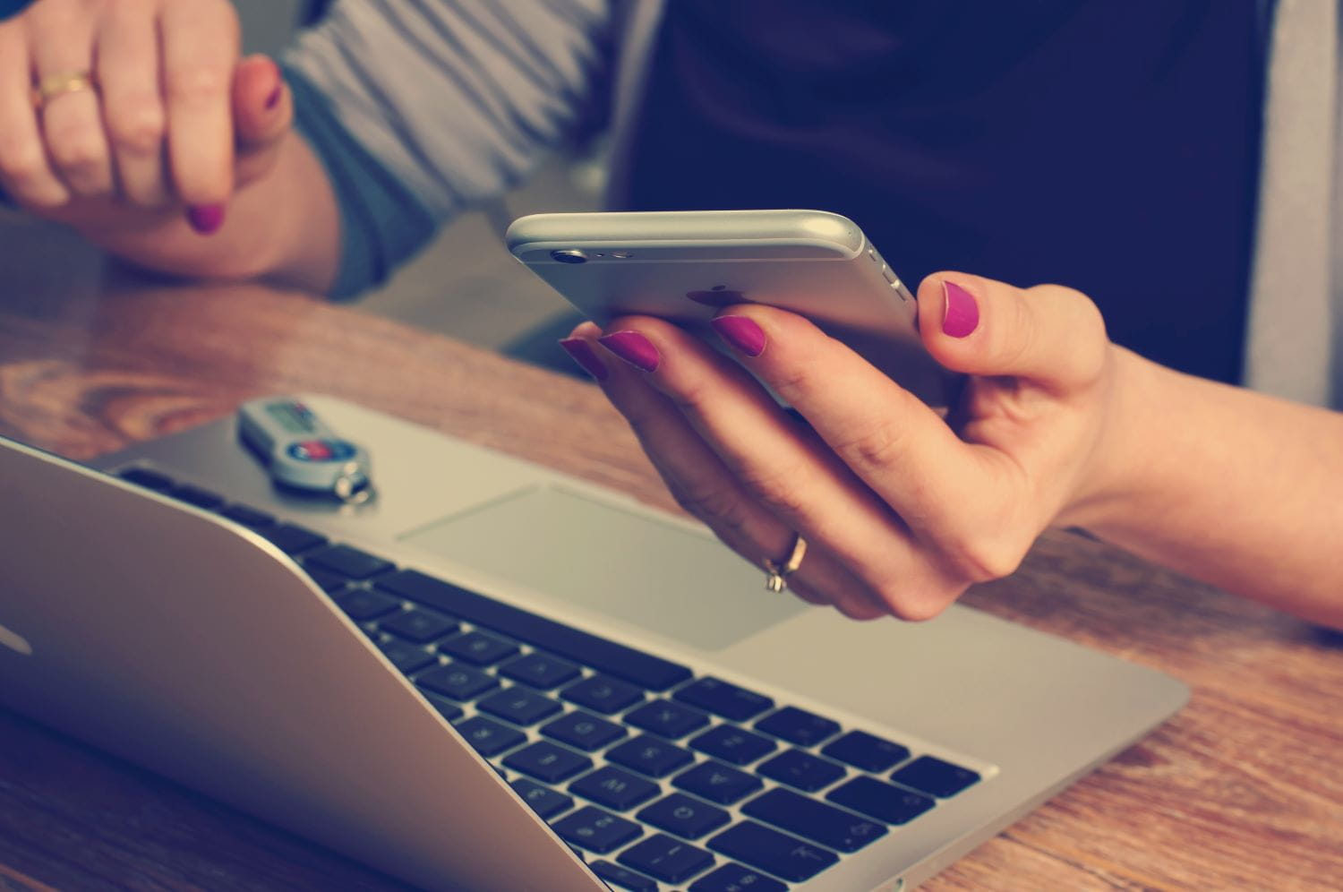 A person sits at a desk on a laptop, with cell phone in hand