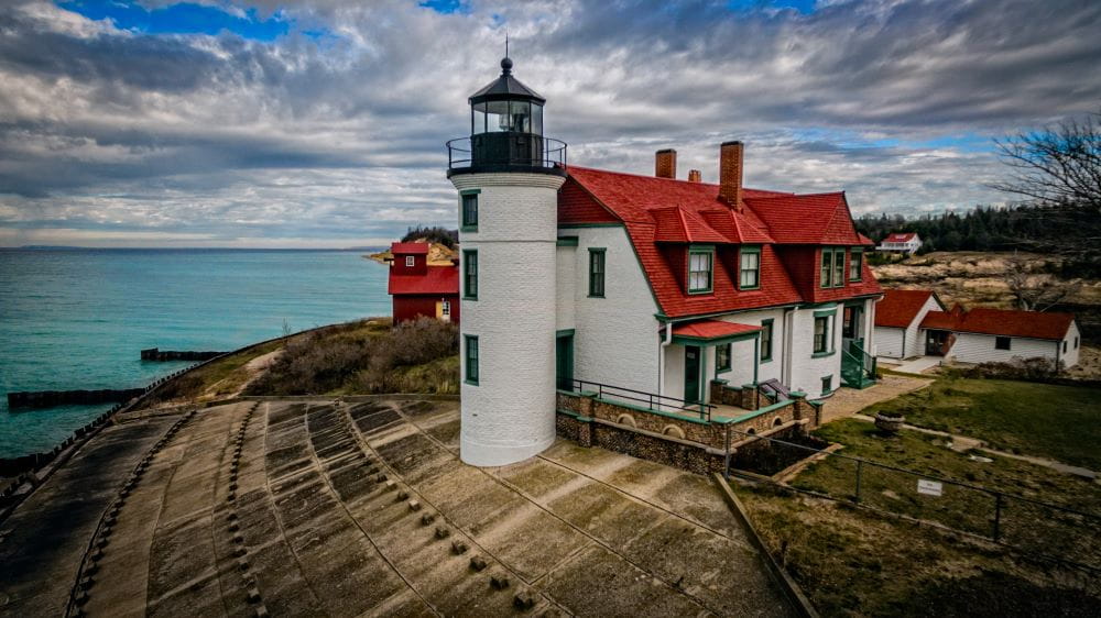 A white lighthouse with red roof on the shore of Lake Michigan, cloudy sky in the background