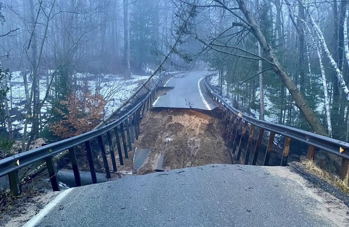 A collapsed roadway bridge over a small stream due to severe flooding