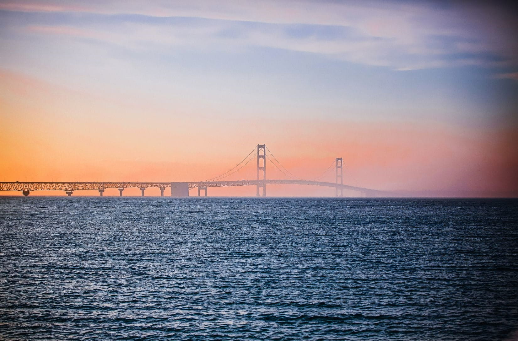 Photo of the Mackinac Bridge and the Straits of Mackinac with a hazy, redish sky.