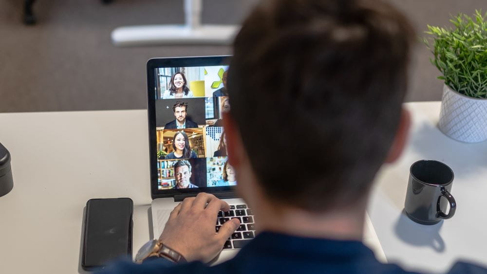 Man sitting down having coffee while looking at a computer screen with other people on it