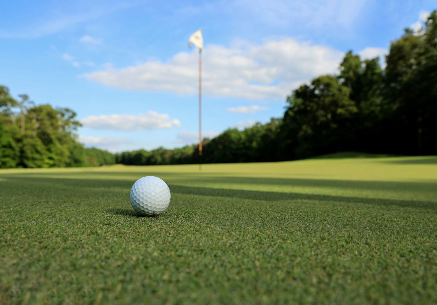 A closeup of a golf ball sitting on turfgrass with a hole and flagstick in the distance