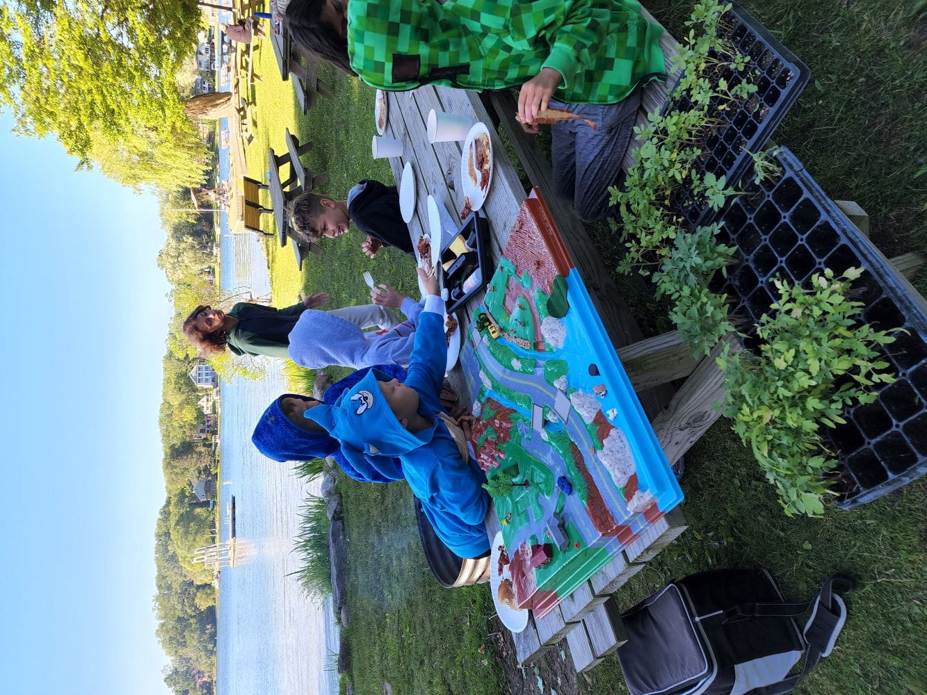 Students from Keith Elementary School sitting outdoors on a picnic table learn about watersheds using EGLE’s Lending Station equipment before planting a native plant buffer.