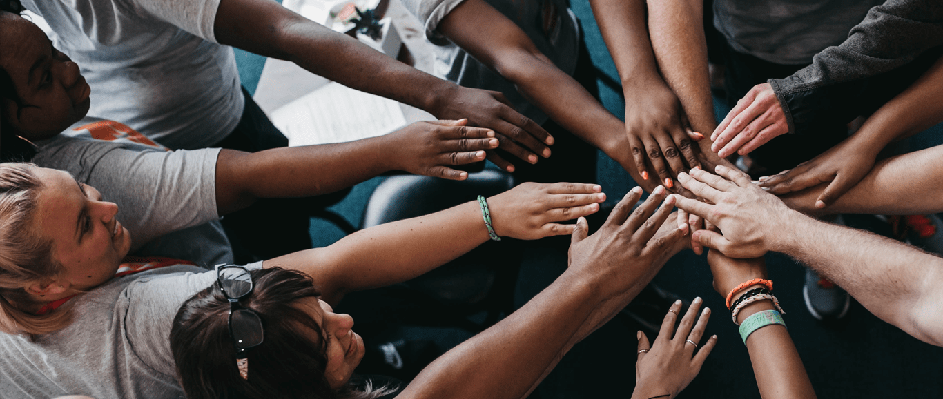 A diverse group of people putting their hands together in a circle for a team huddle
