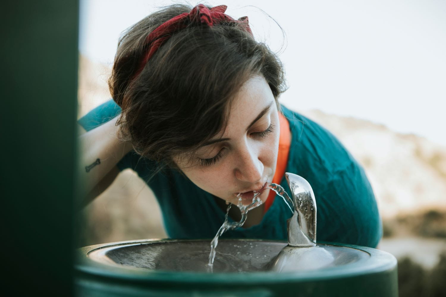 A person holding their hair back, drinking water at a drinking water fountain