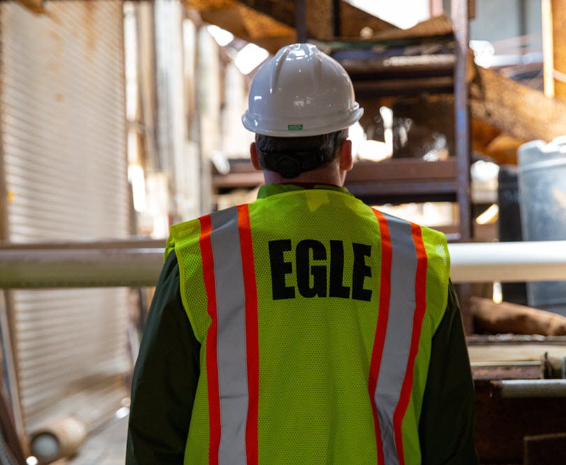 back of person in safety vest and hard hat looking out at a cluttered warehouse