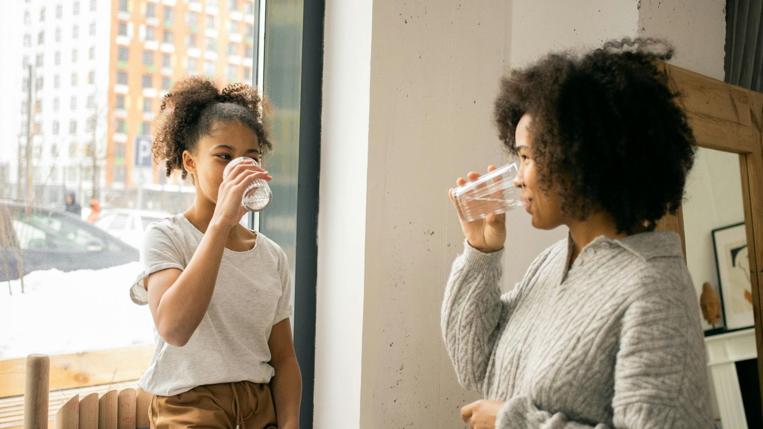 A young child and their mother smiling while drinking glasses of water