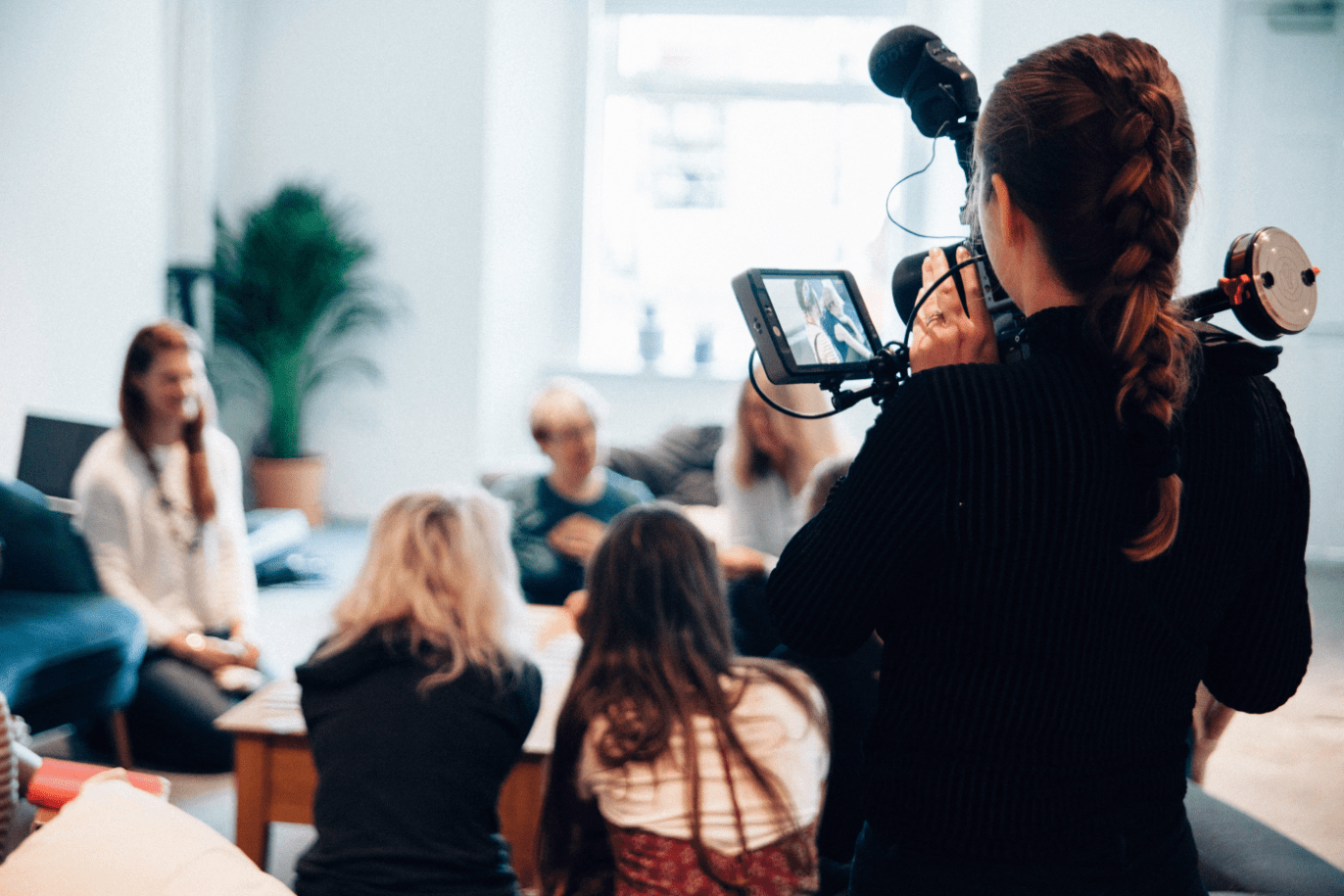 A woman stands with a camera and microphone, recording an interview