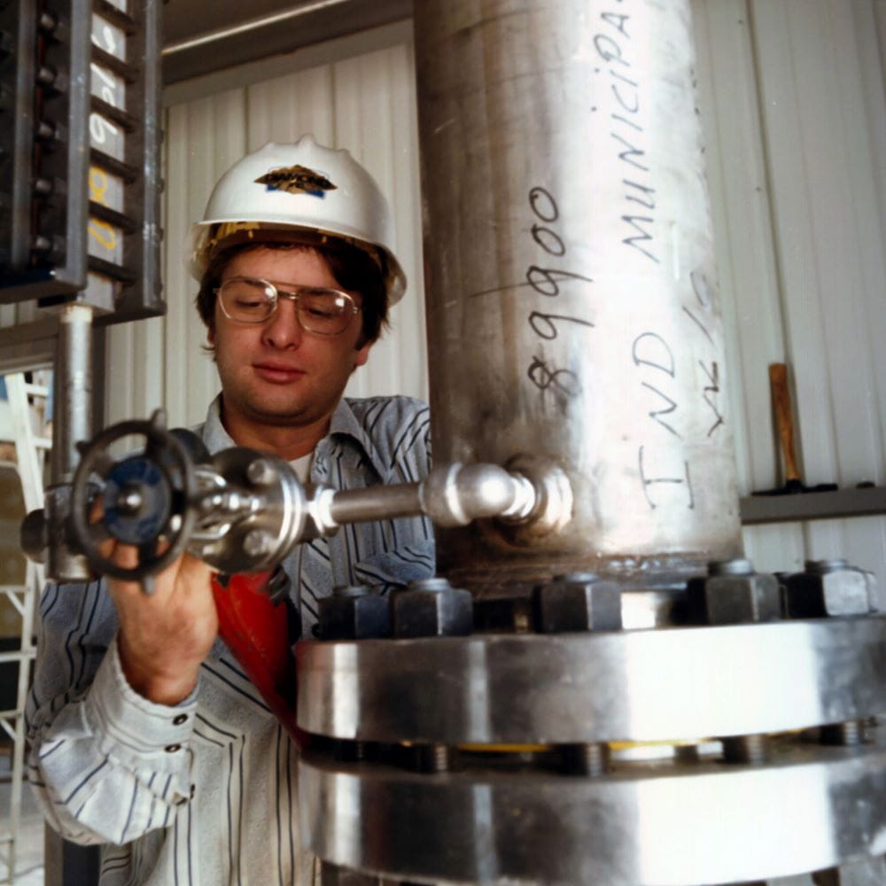 A man wearing a hardhat standing by a large metal pipe
