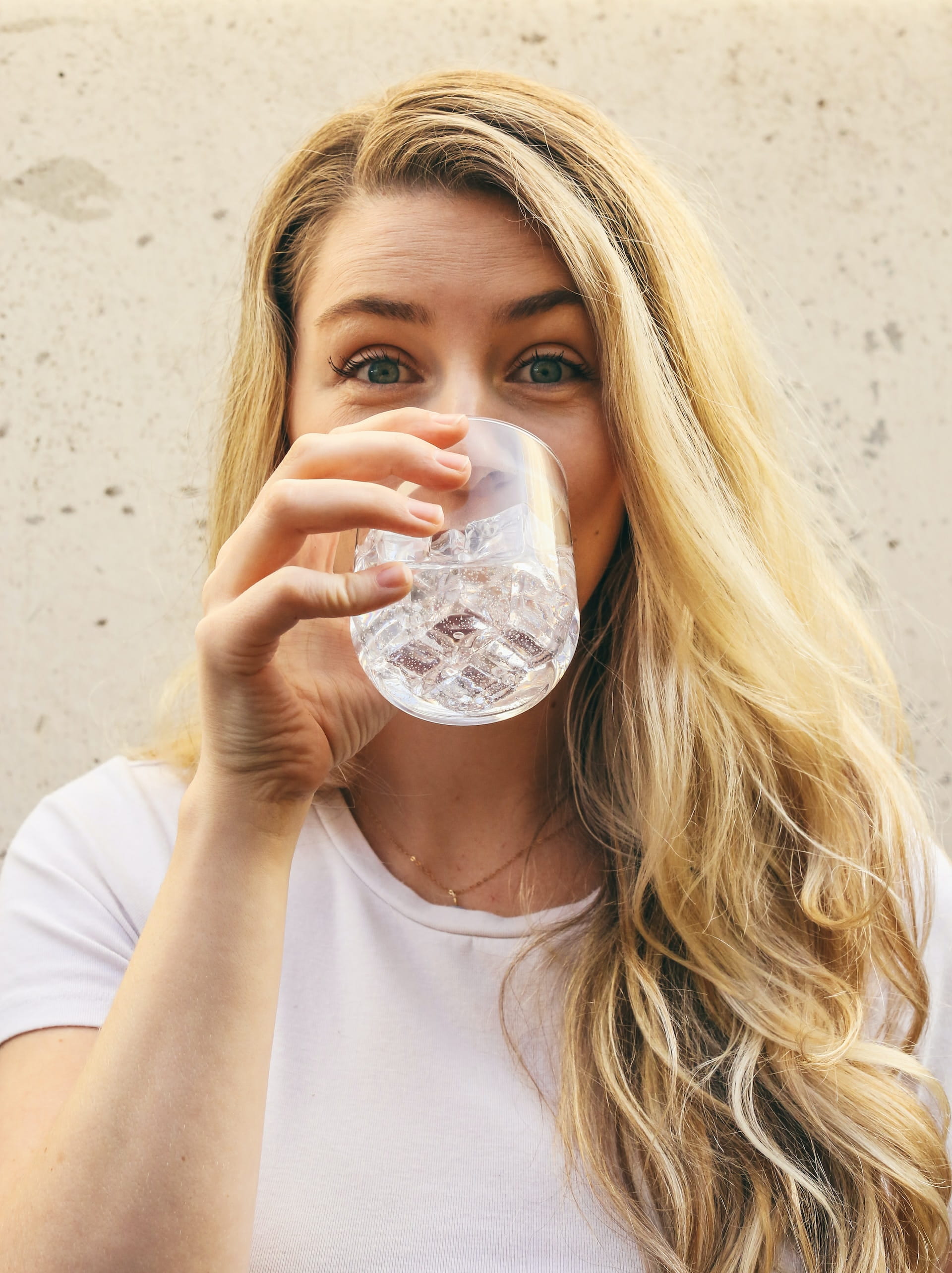 A woman with blonde hair drinking a glass of water