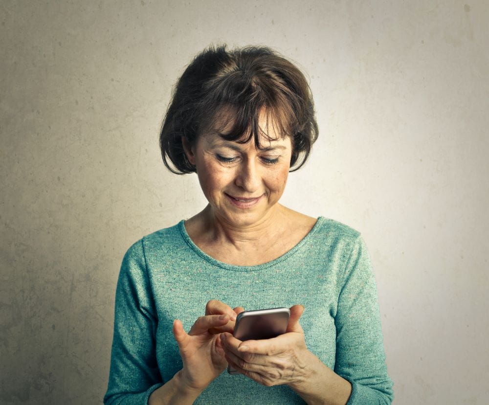 A older adult woman in a green sweater with a smartphone in hand