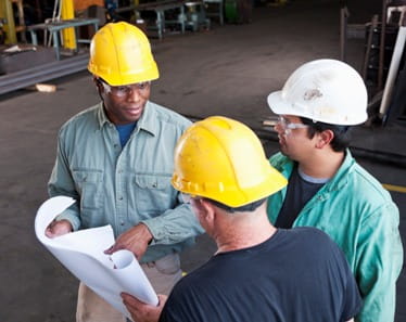 Three men in hardhats having a discussion in a manufacturing facility