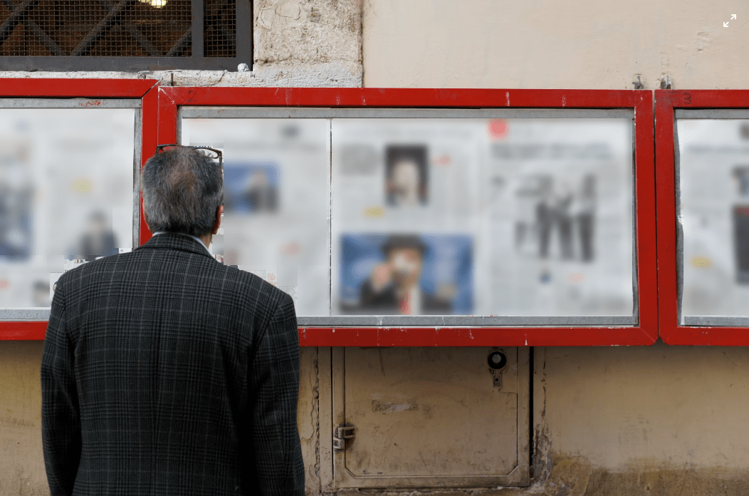 An adult man looking at a wall with a newspaper posted
