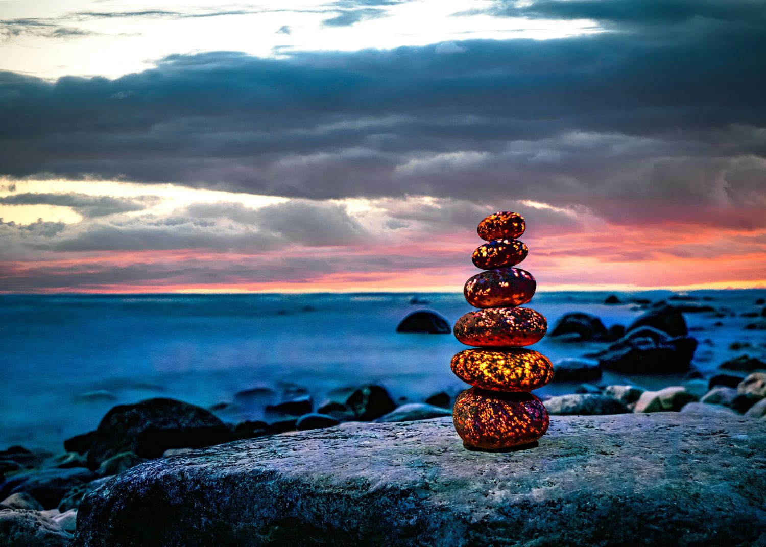 A stack of rocks on a lakeshore at sunset; the stones have glowing yellow flecks