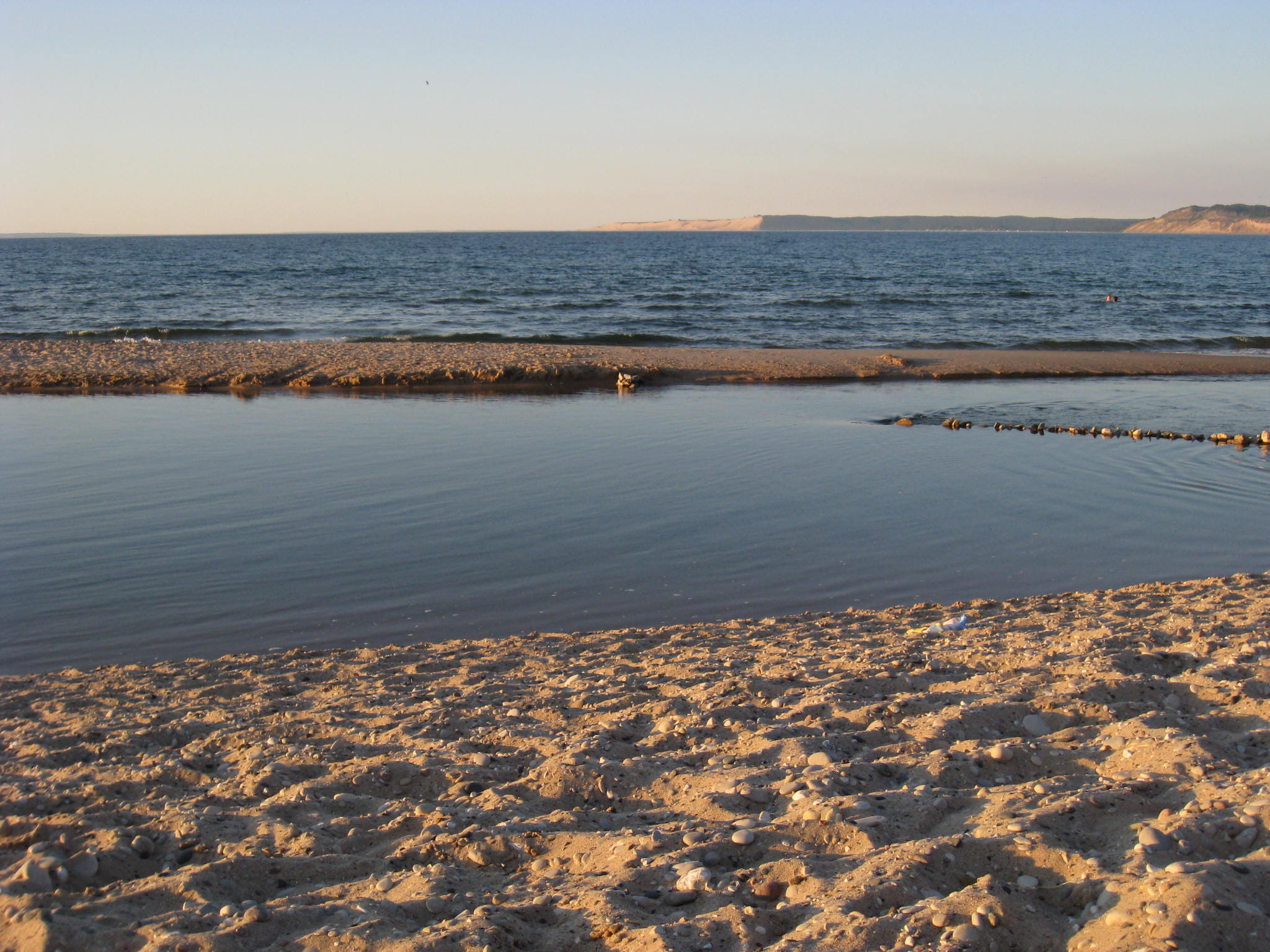 Shoreline along Lake Michigan, with sand dunes in the distance and sand/pebbles in the foreground