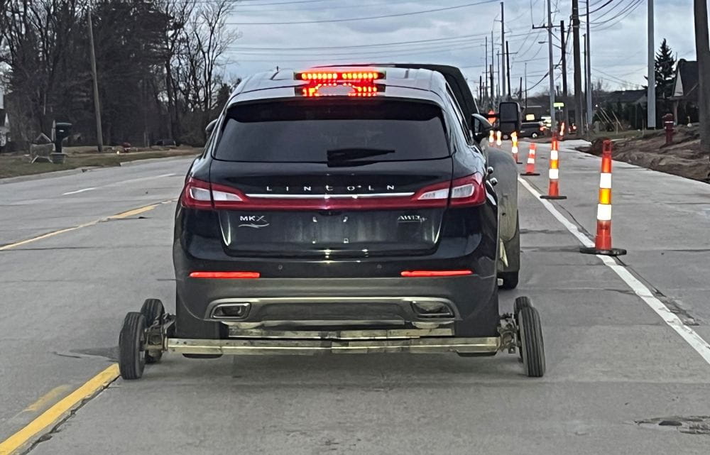 Trailer with tires in poor condition on a Michigan road hauling a car.