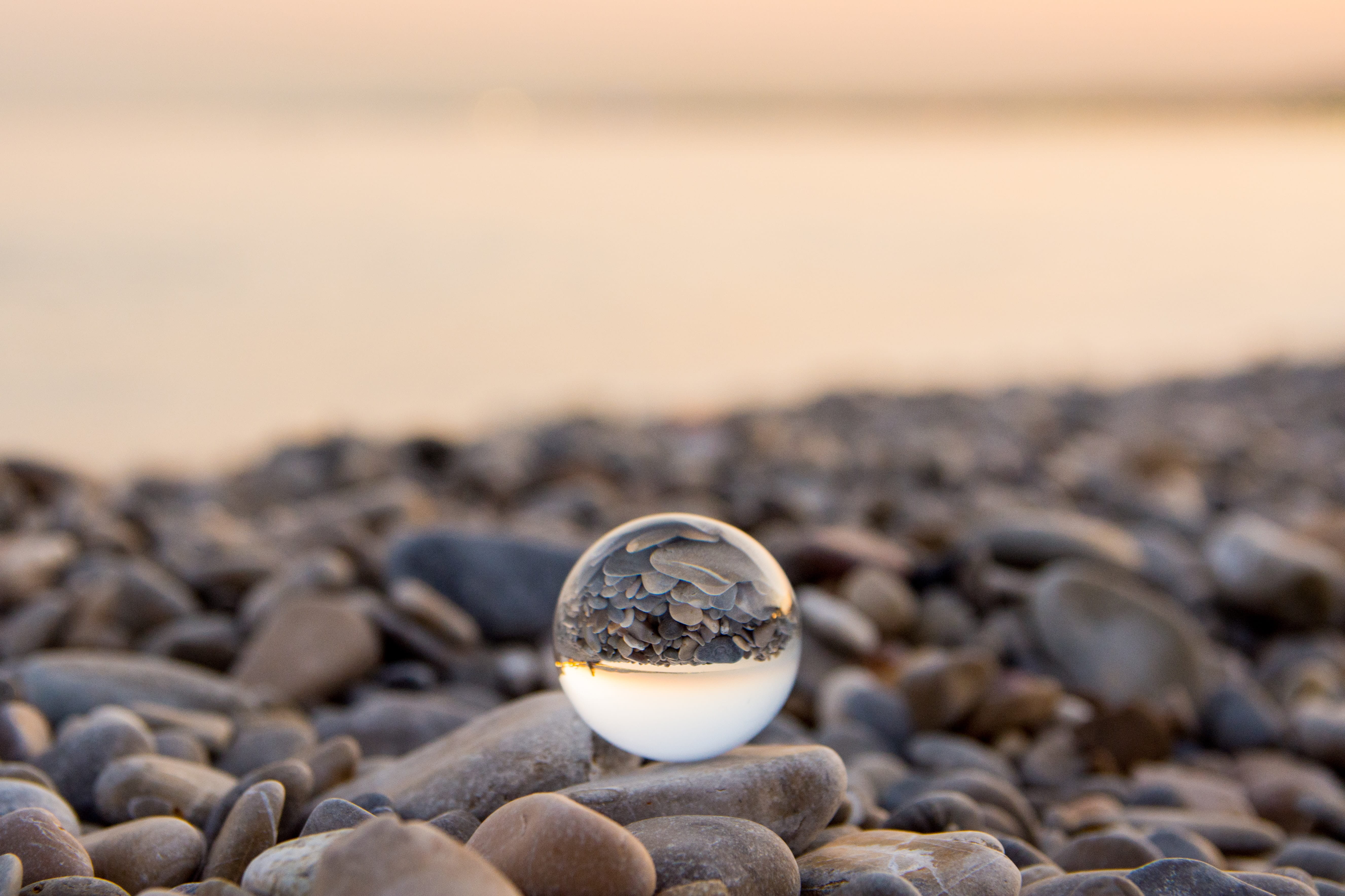 A glass ball resting on a serene beach of pebbles with a lake in the background