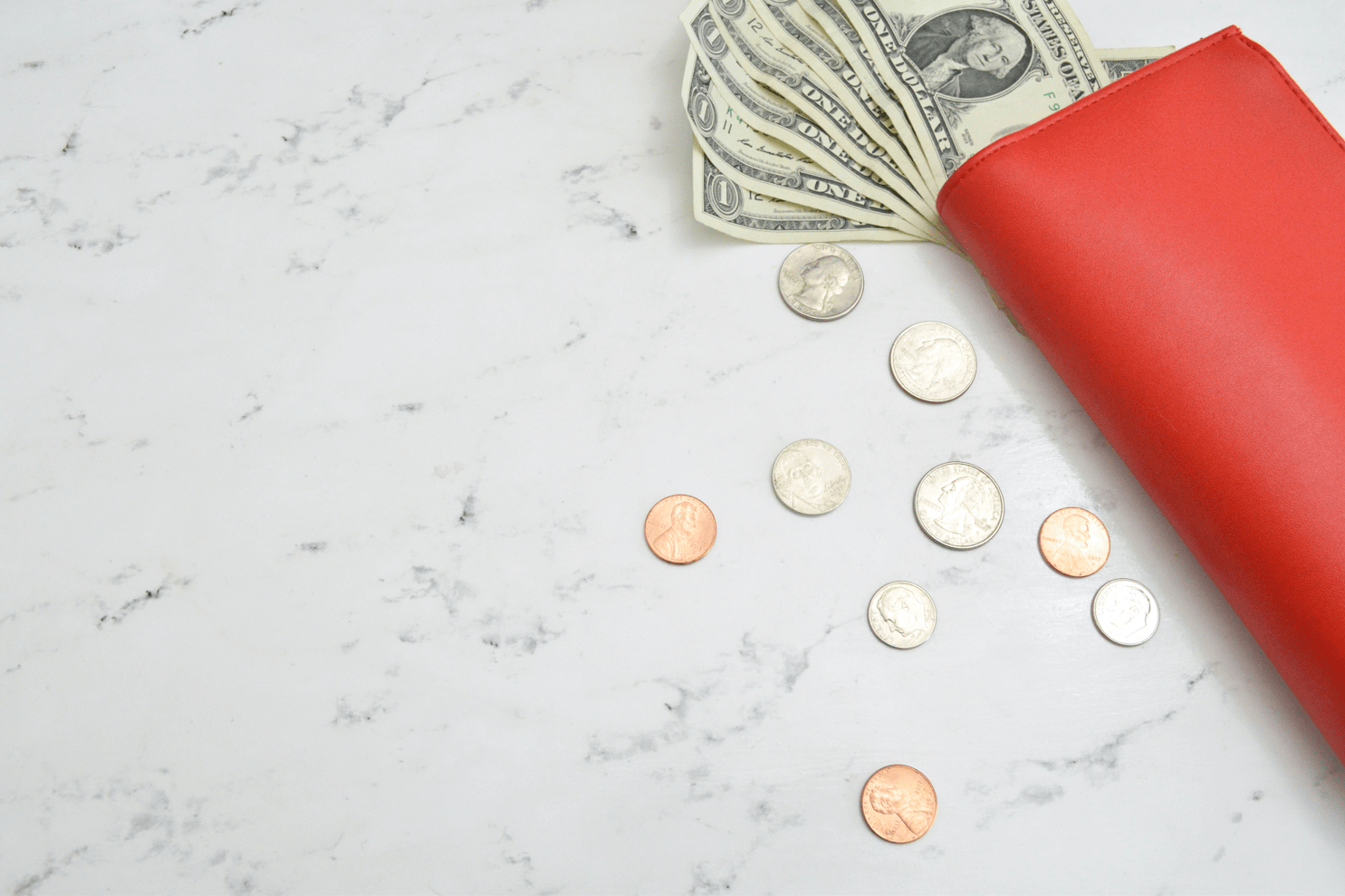 A red wallet with several dollar bills peeking out, and coins scattered on the table