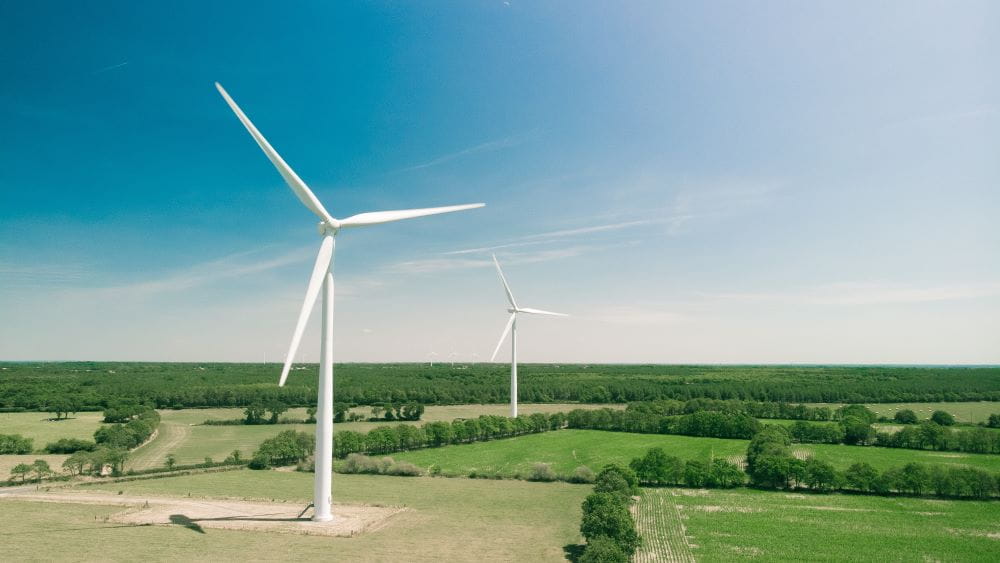 A wind turbine stands tall above green farm fields and a clear blue sky