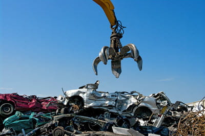 The claw of a large crane hovering over a pile of junk cars with blue sky in background