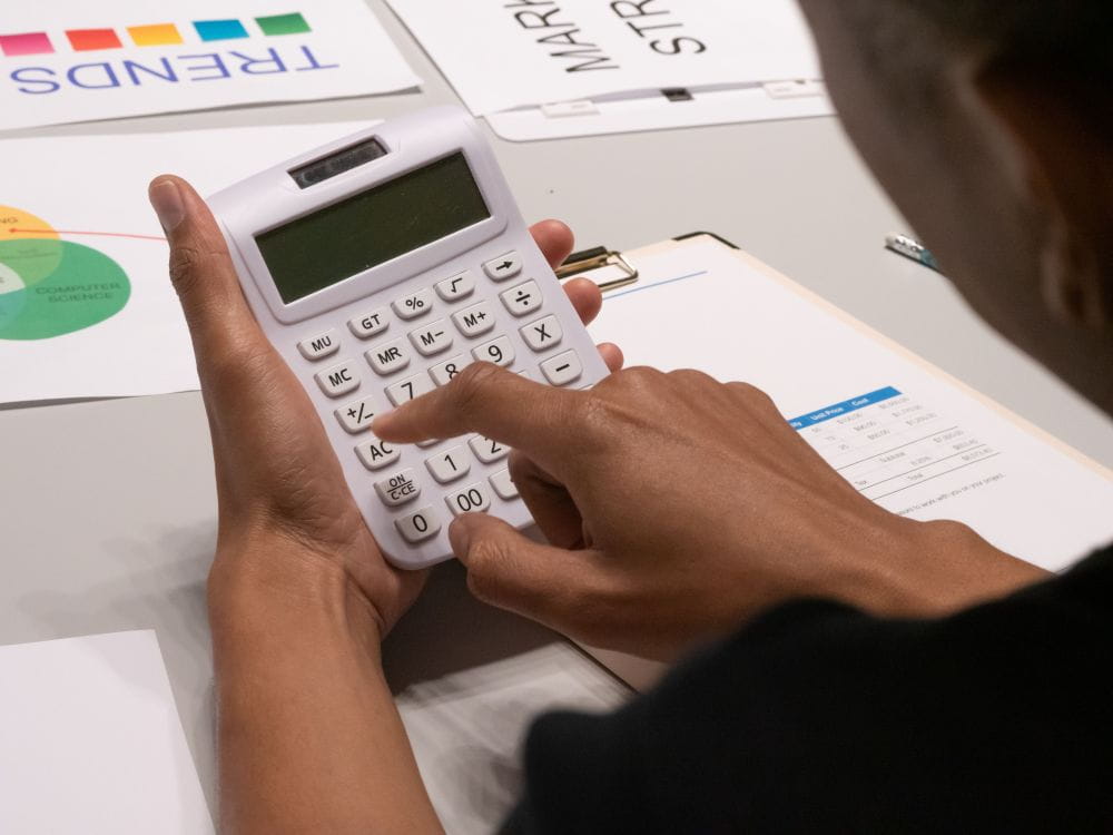 Woman entering numbers on a calculator, with papers scattered on a table.