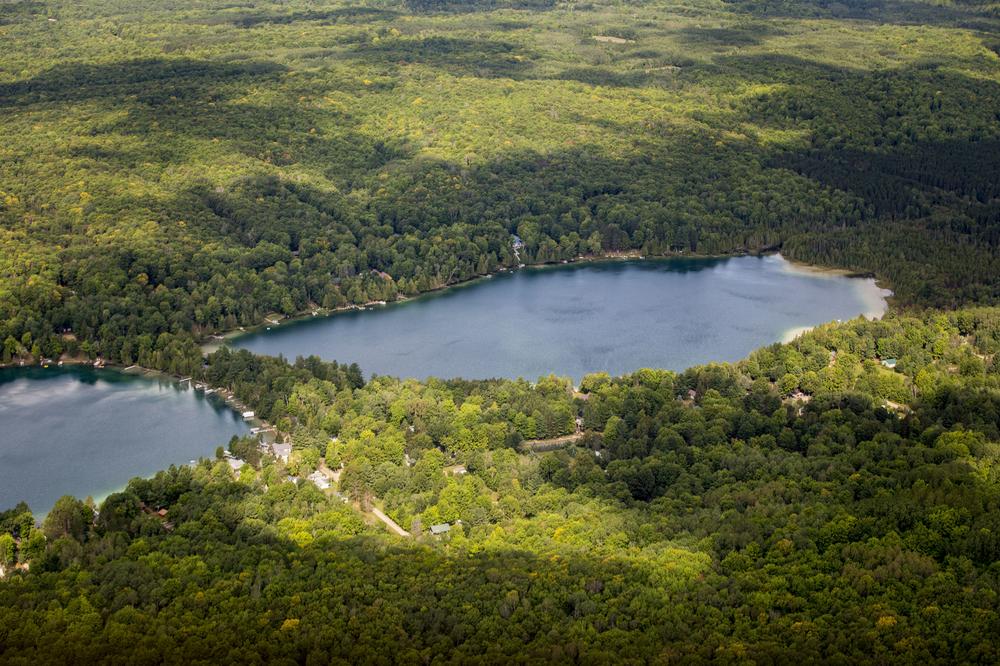 An aerial view of a northern Michigan forest. Green trees in all directions with an inland lake in the middle