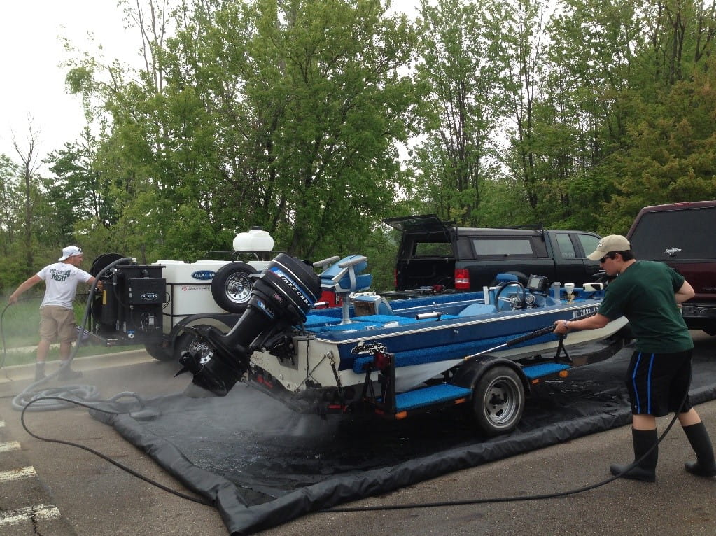 Two students & Mobile Boat Wash crew members clean a boat at Lake Ovid