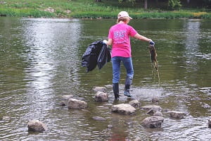 A woman cleaning a river, tossing trash into a bag.