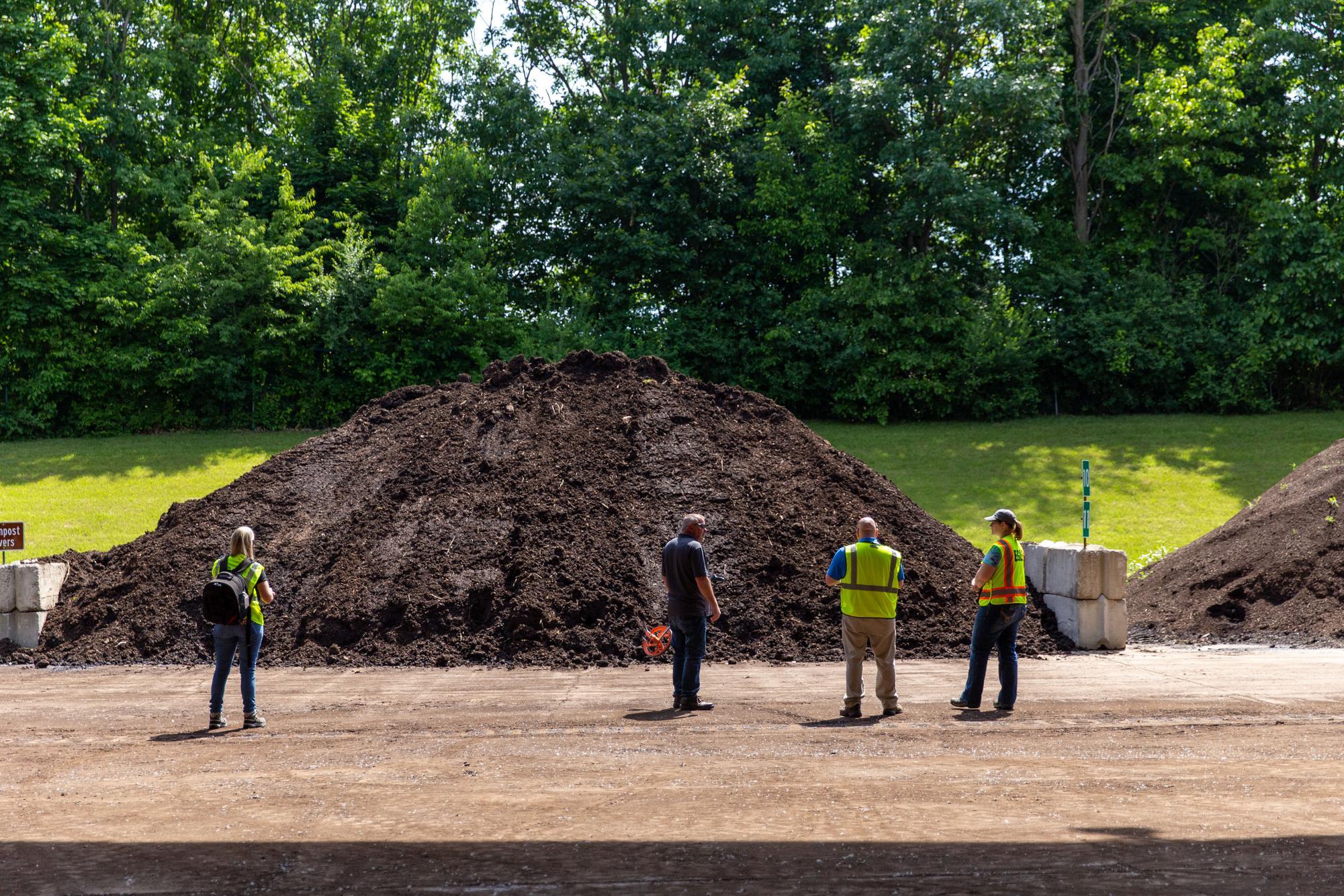 EGLE staff in fluorescent yellow vests standing with a wastewater treatment plant operator, looking at a large pile of rich brown compost towering over them