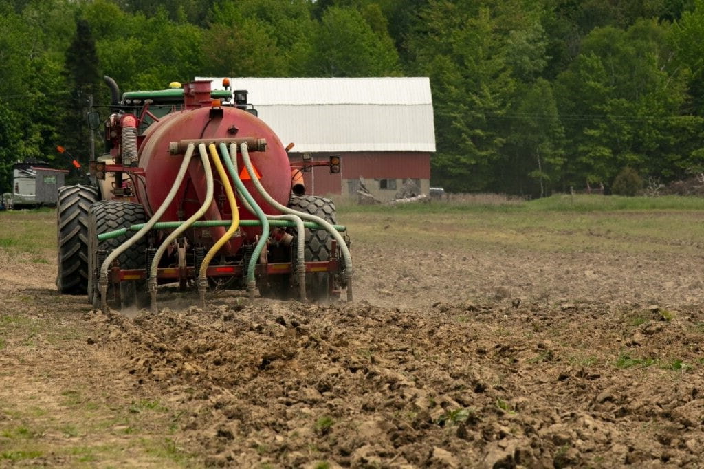 A large machine called a TerraGator driving through a farm field, spraying biosolids directly on the ground through 6 hoses on the back
