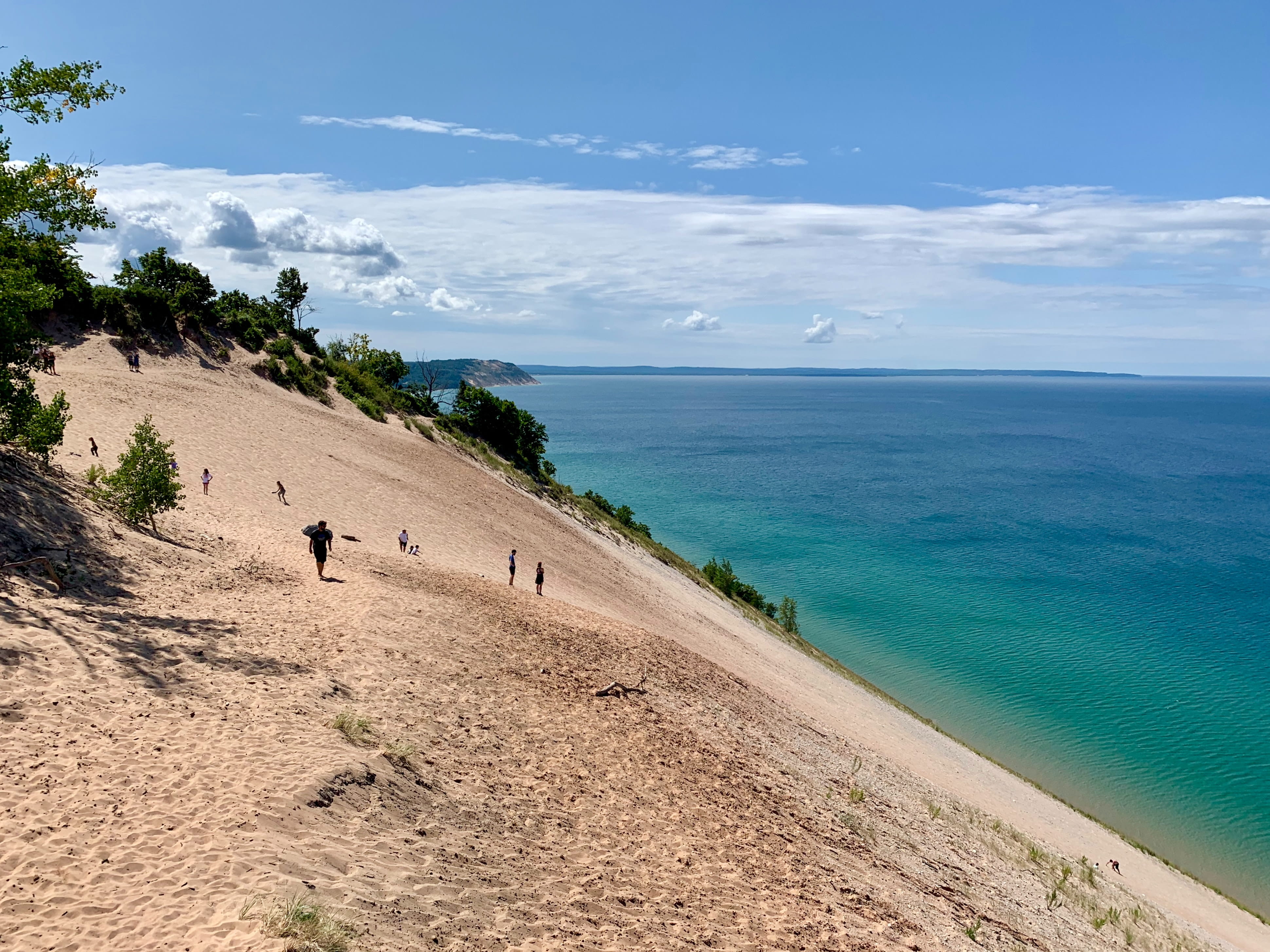 An extremely steep sand dune at Sleeping Bear Dunes National Lakeshore; the sky is blue and the turquoise Lake Michigan in the background is sparkling
