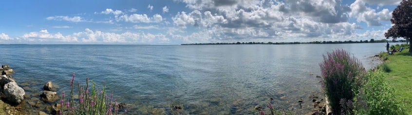 Lake St Clair with bright blue sky, clear water, green grass along a rocky shore and people fishing