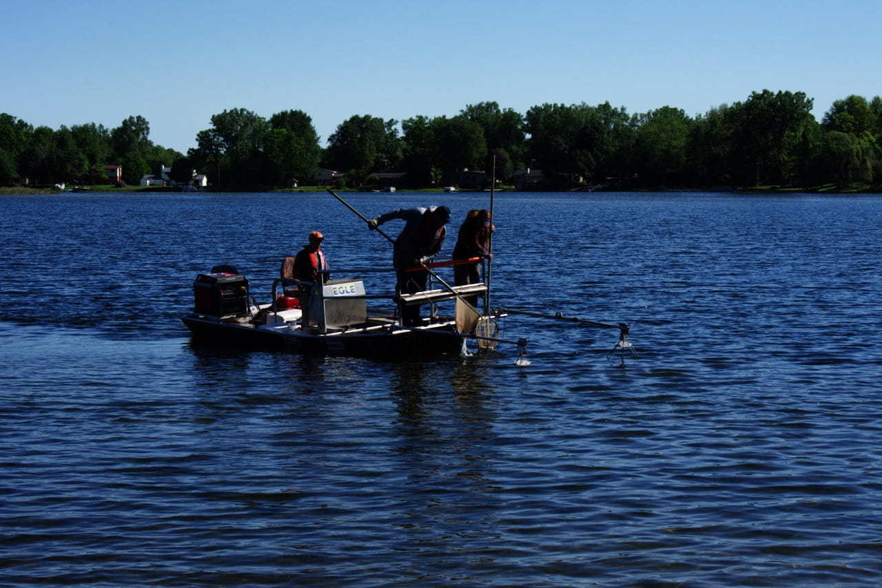 Three EGLE staff on a small boat conducting electrofishing using specialized equipment to gather fish to sample and help assess water quality