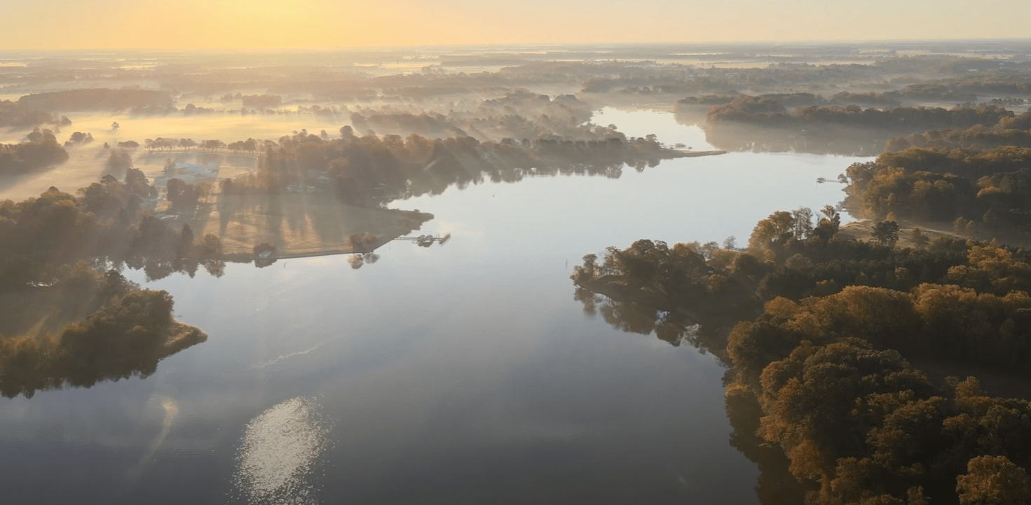 A brilliant aerial view of a river in the morning sunshine, with fog covering the ground and sun rays piercing through