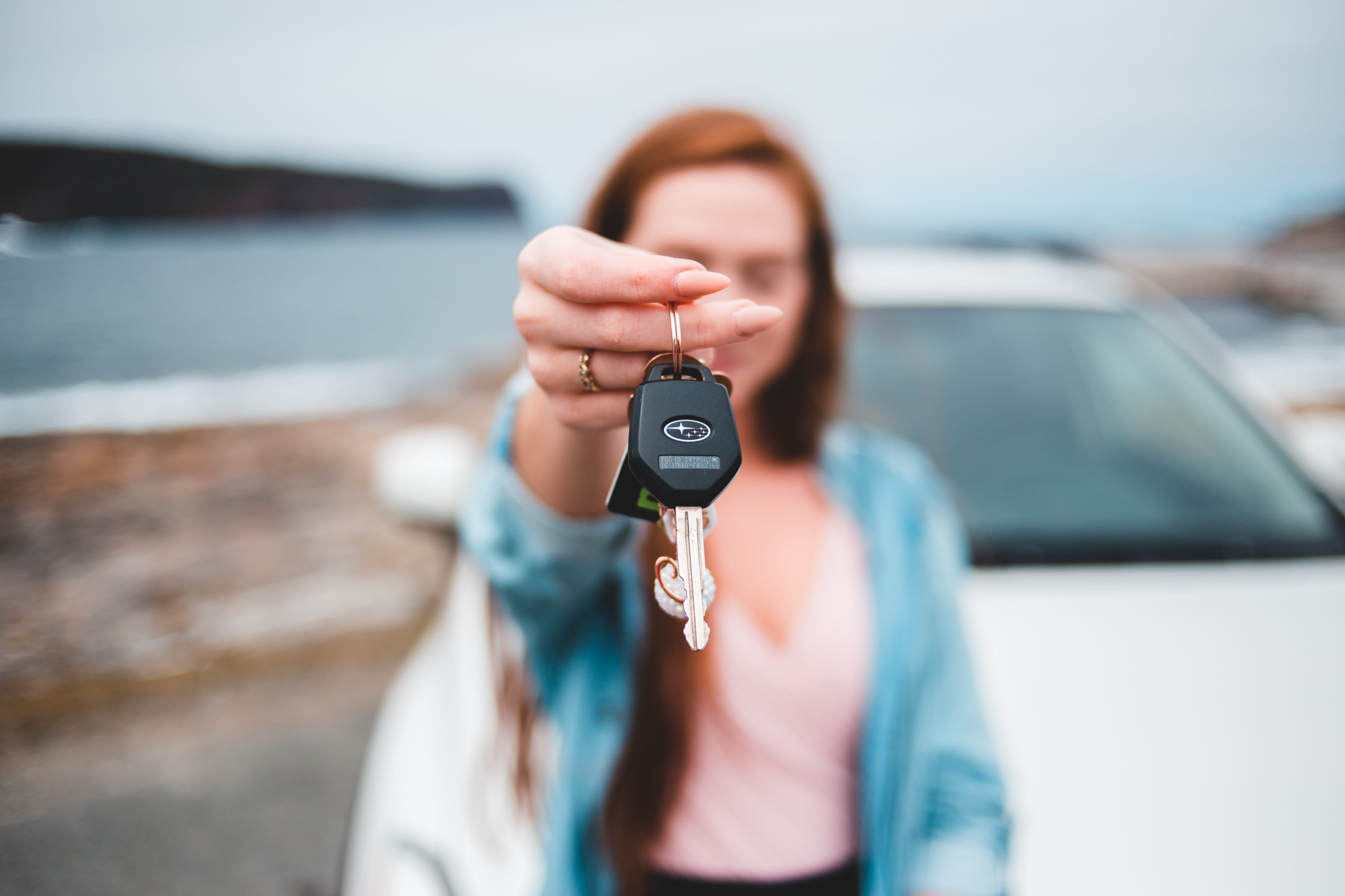 Photo of a woman standing in front of her car holding up her car keys.