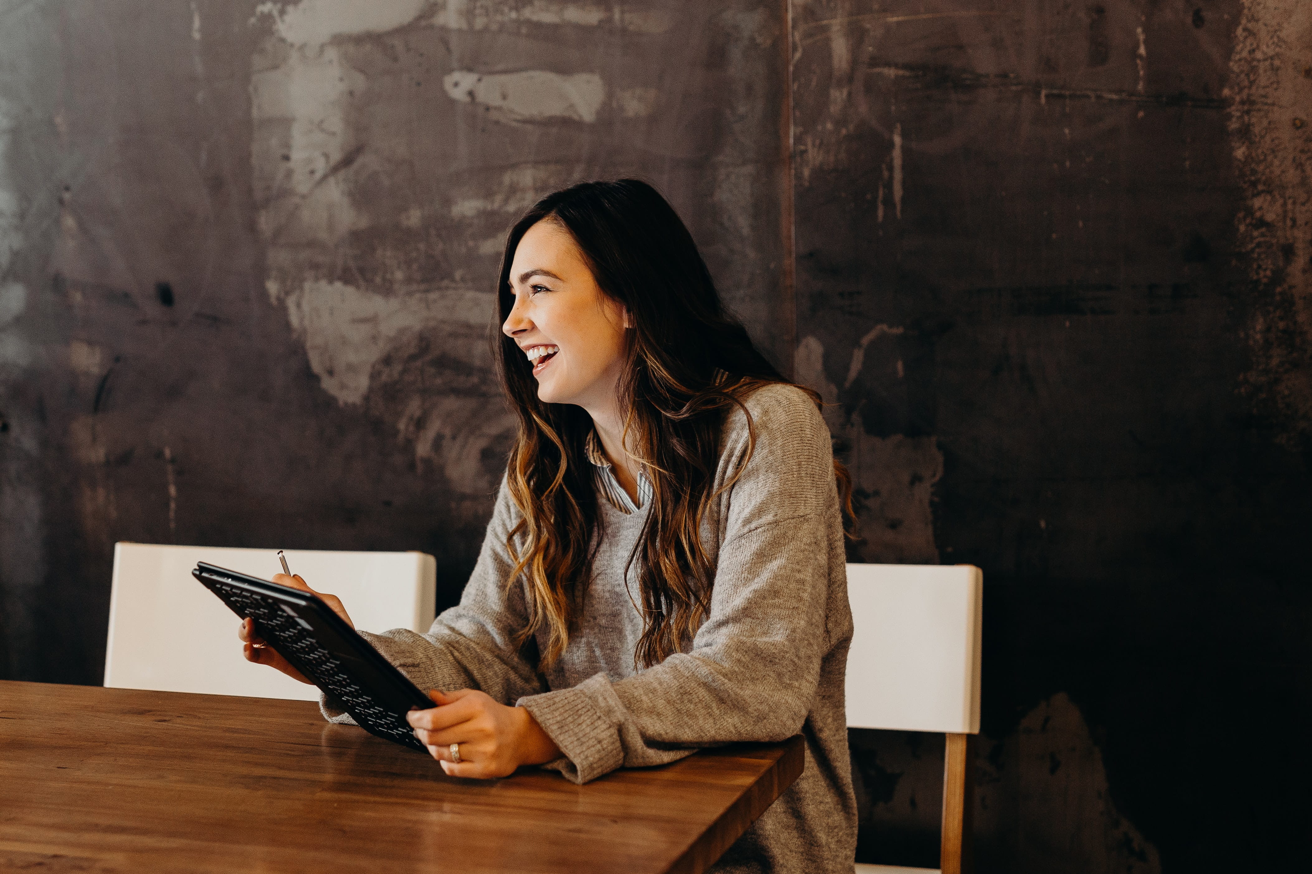 Photo of a woman sitting at a table holding a tablet.