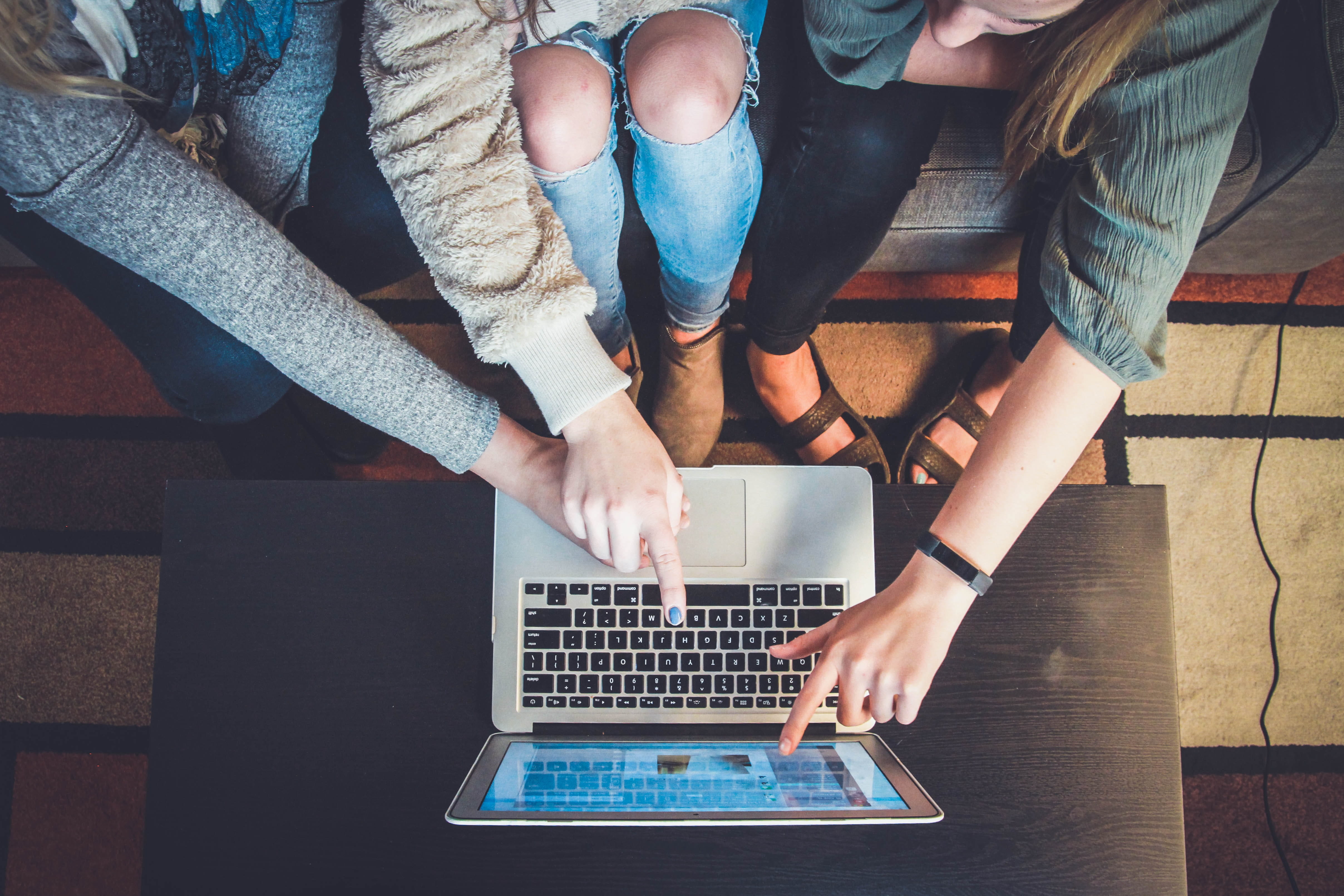 Photo of a laptop with three people gathered around it.