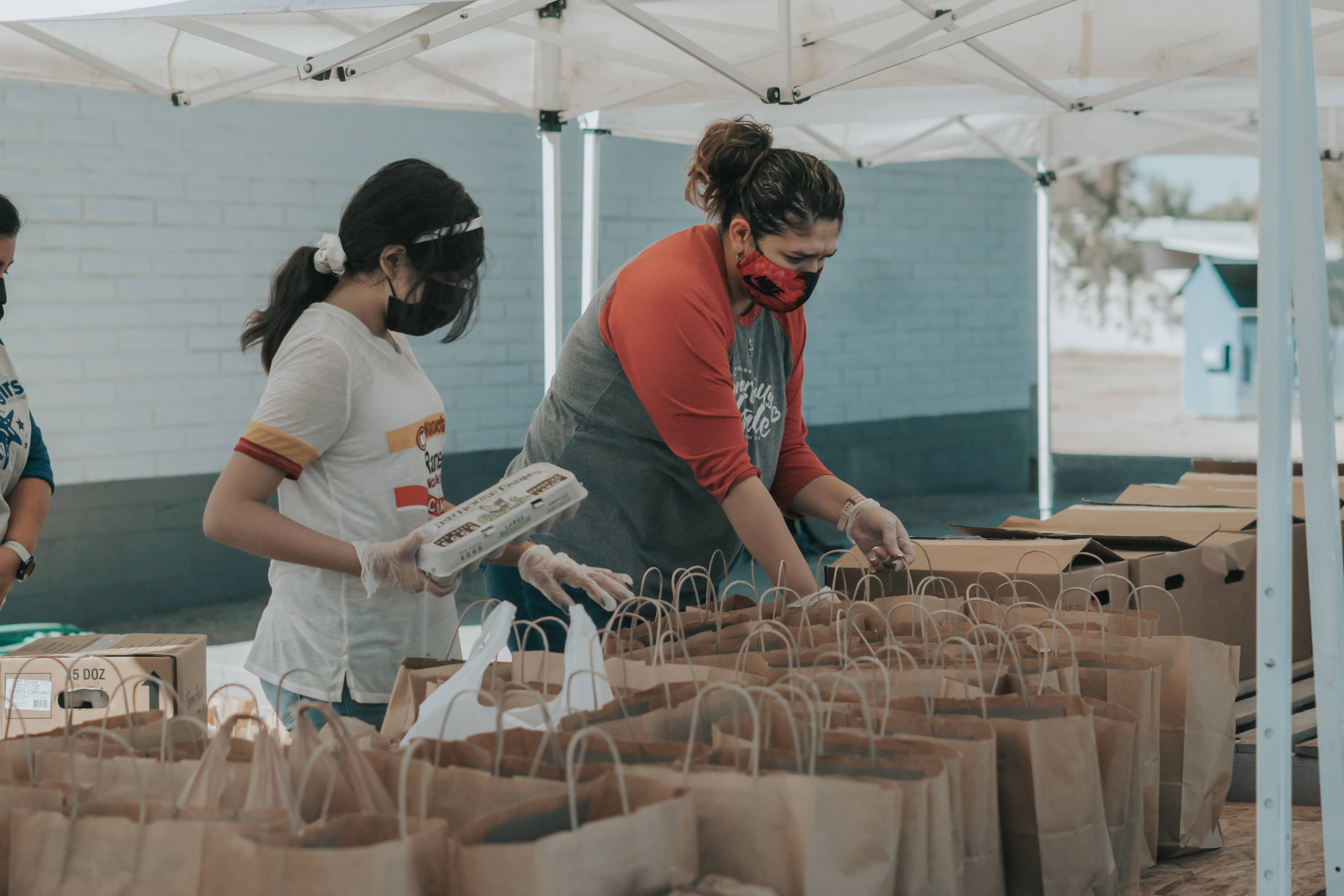 Photo of two people volunteering at a food bank, packing bags with food.