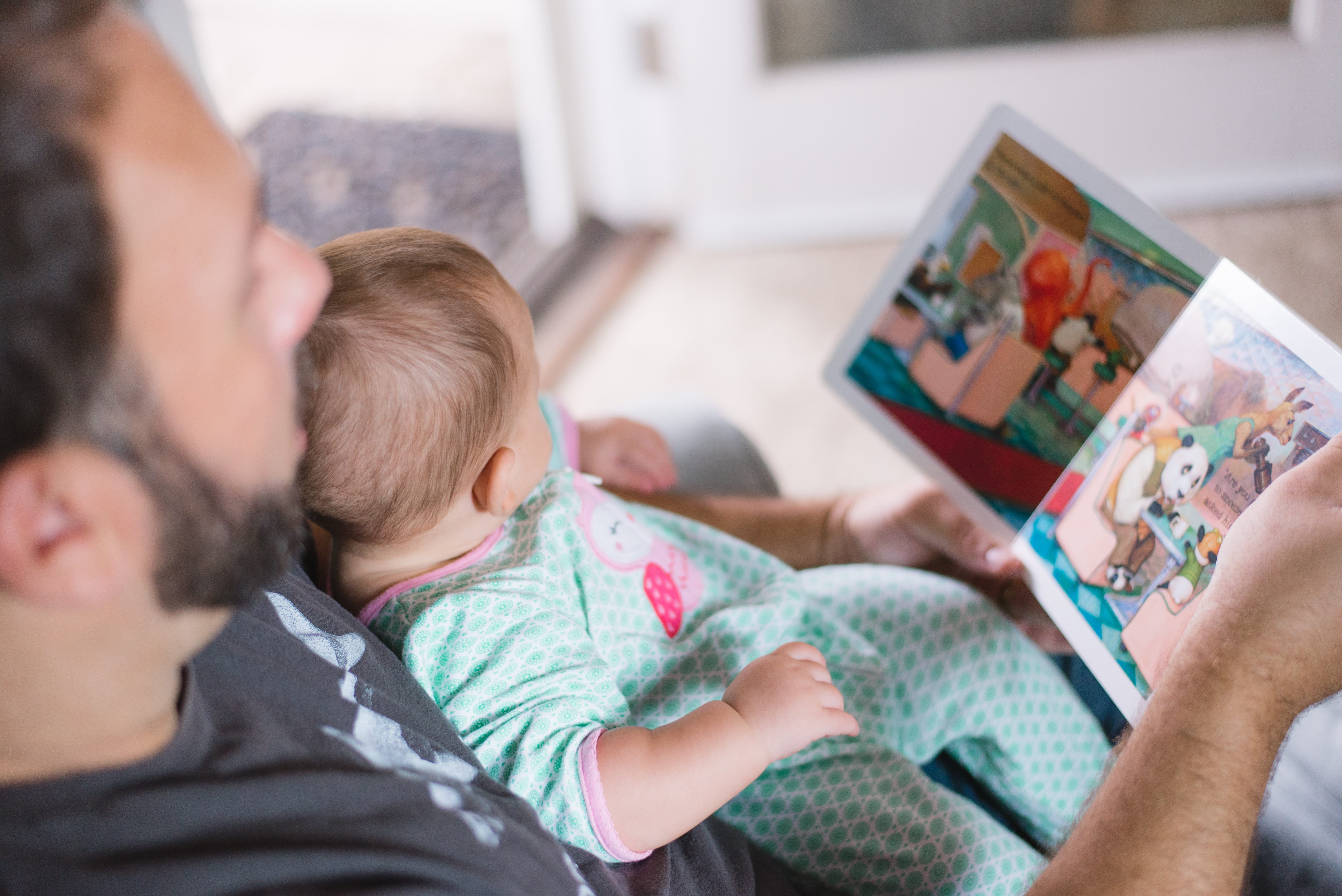 Photo of a father reading a book to a baby.