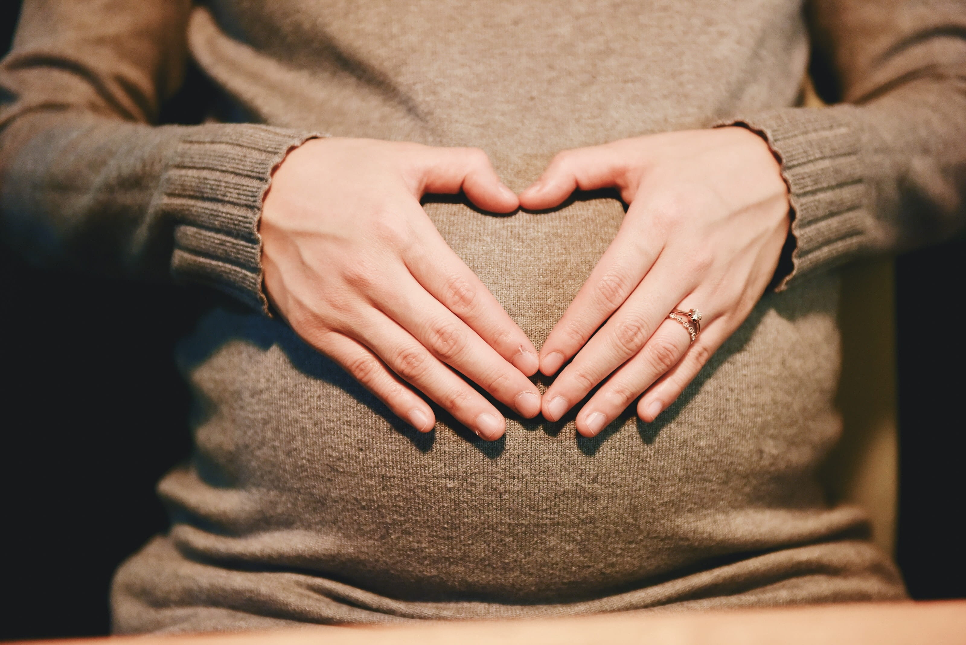 Photo of a pregnant woman with her hands on her stomach in the shape of a heart.