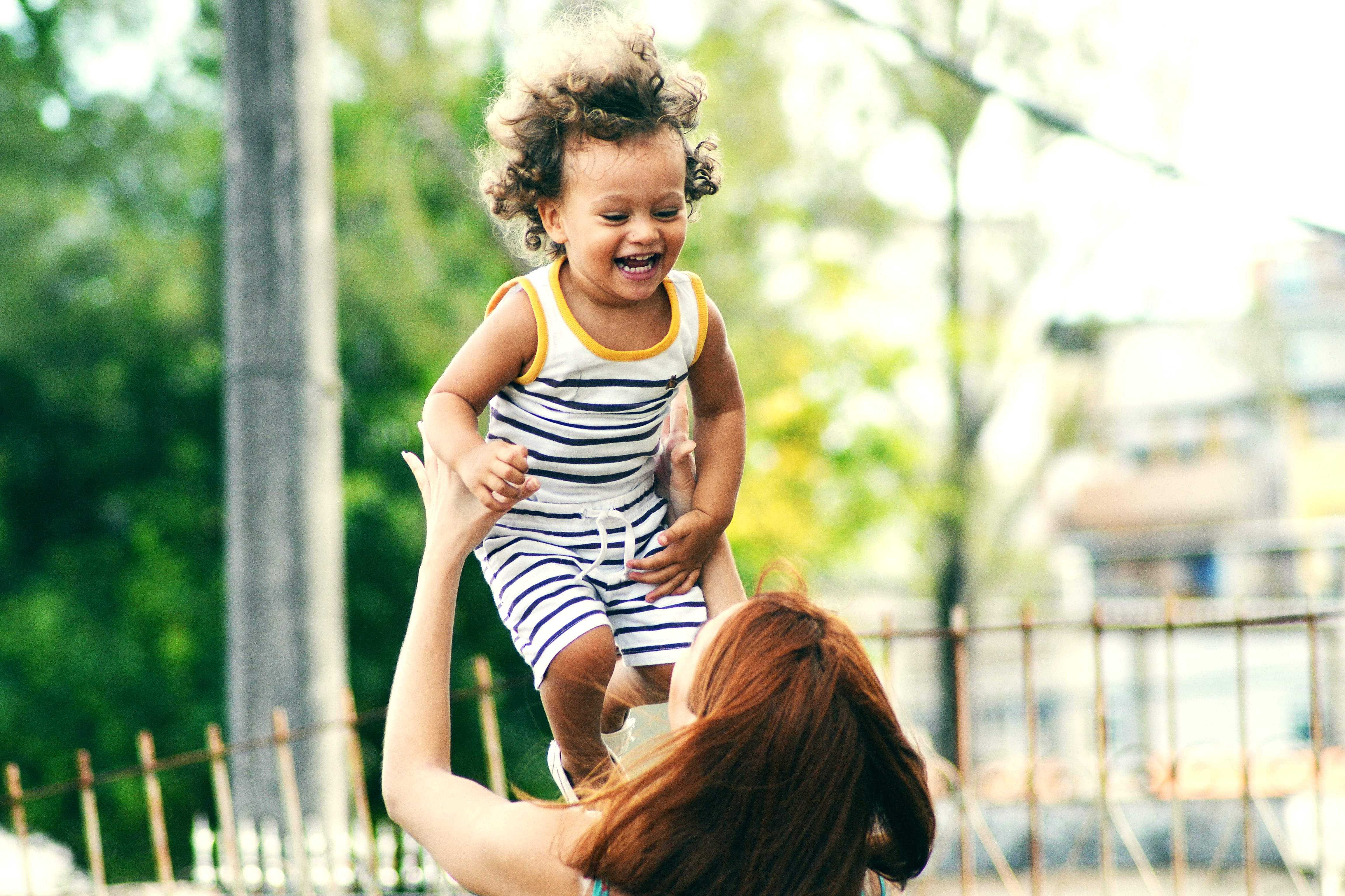 Photo of a mother holding her toddler in the air as he laughs.