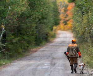 A hunter walks down a dirt road in the PRC with his dog