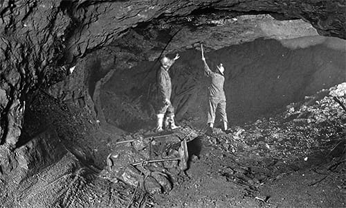 Two miners wearing hard hats inspect the ceiling of an iron ore mine Two miners wearing hard hats inspect the ceiling of an iron ore mine